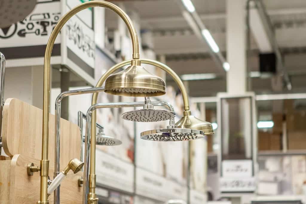 Close-up view of several modern showerheads with metallic finishes displayed in a store, highlighting the importance of choosing high-quality materials for your remodel project. Shelves and lighting are visible in the background.