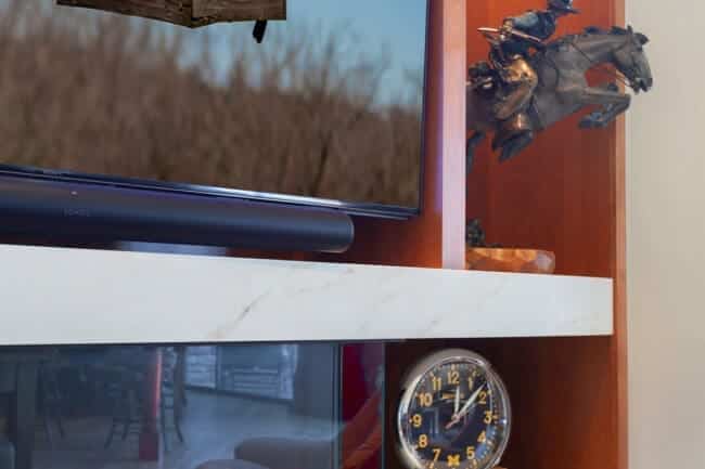 A living room shelf with a TV displaying a birdhouse and cardinal, a dragon sculpture, a round clock, and an aquarium with red fish below creates the perfect fireplace built-in feature for cozy and stylish decor.