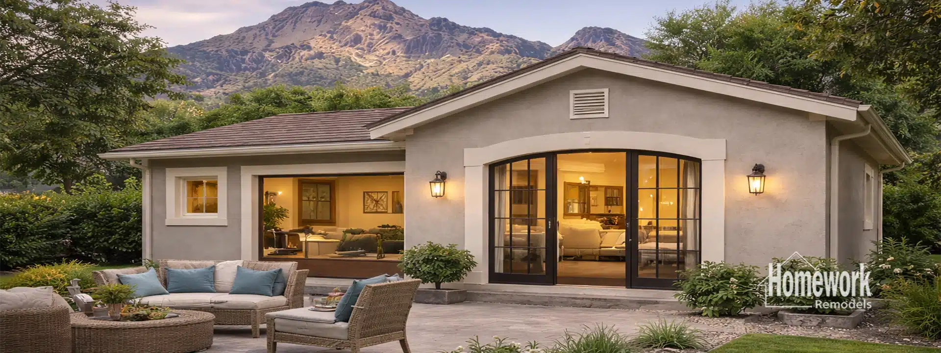 A cozy, modern Casita Addition features large glass doors and windows set against a mountain backdrop. Outdoor seating and greenery decorate the patio. The Homework Remodels logo appears in the bottom right corner.