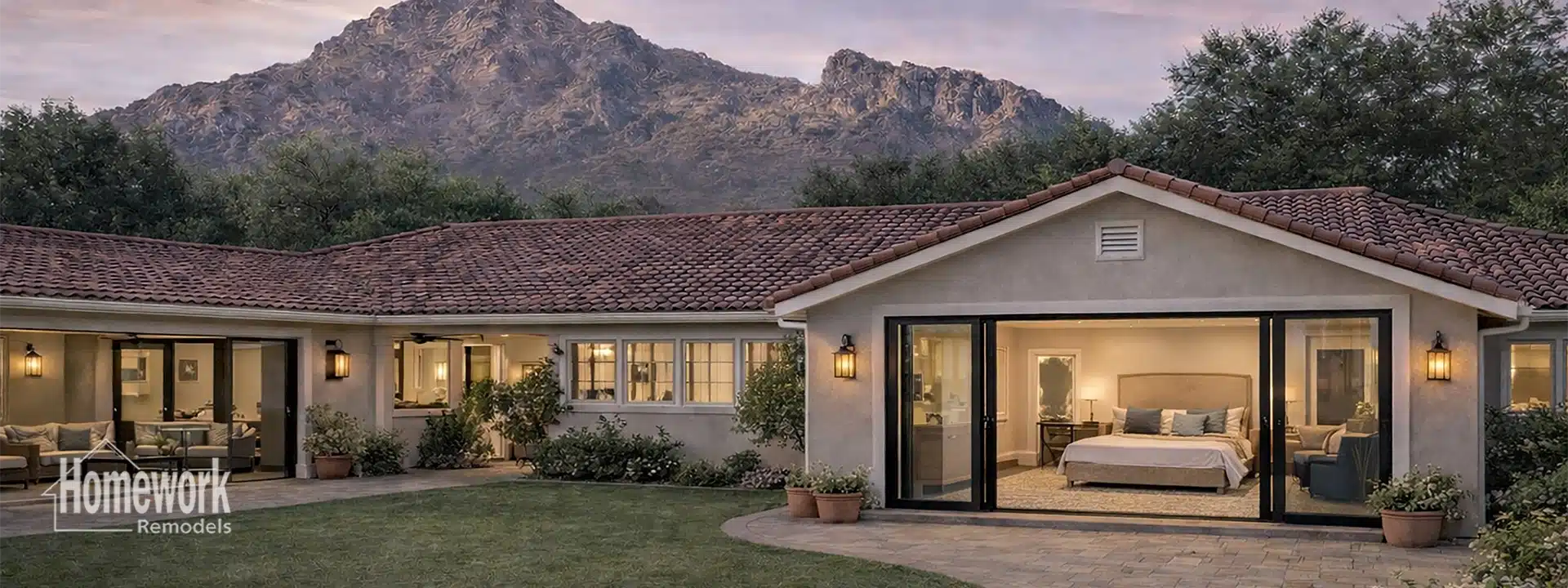 A single-story home in Arcadia with large windows and a tile roof sits in a landscaped yard, with a mountain backdrop at sunset. The image displays the Primary Suite Additions interior through sliding glass doors. Homework Remodels logo is visible.