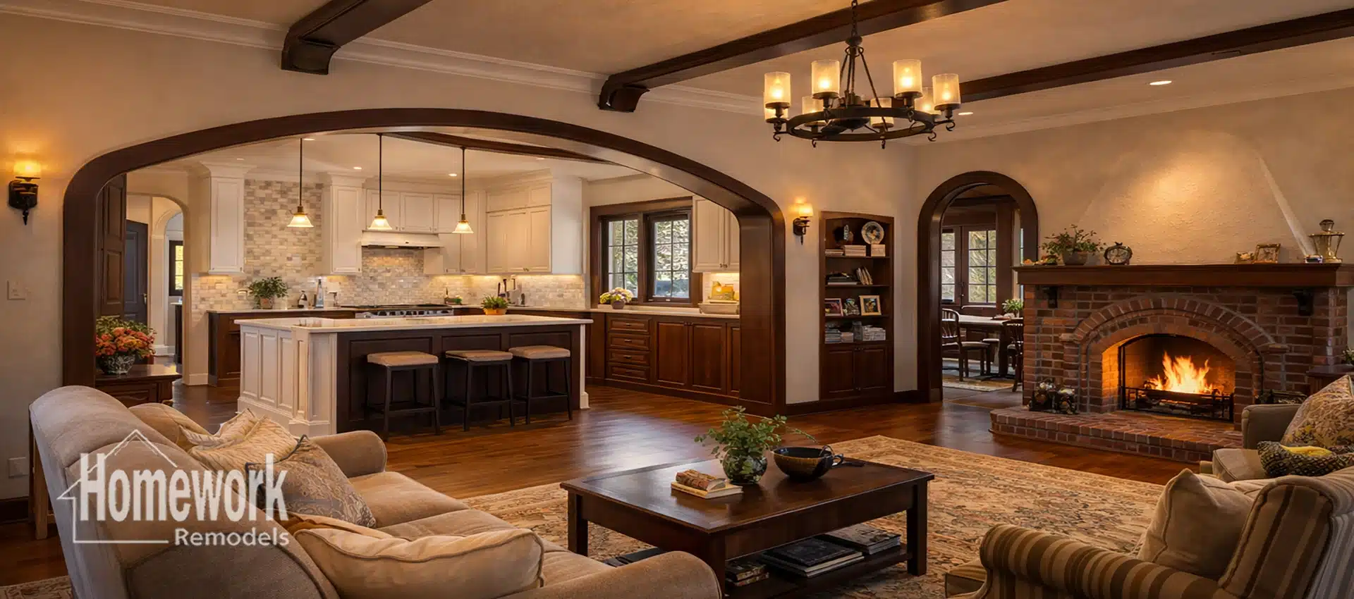 A warm, inviting living room with a lit fireplace, wooden beams, and arched doorways leads to a Willo open concept kitchen featuring a large island and barstools. The space is cozy and tastefully decorated.