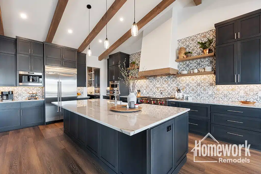 Modern tempe kitchen with dark cabinets, a large marble island, stainless steel appliances, and patterned tile backsplash. Featuring sustainable remodeling materials, wooden ceiling beams, pendant lights, open shelving with decor. Homework Remodels logo in bottom right corner.