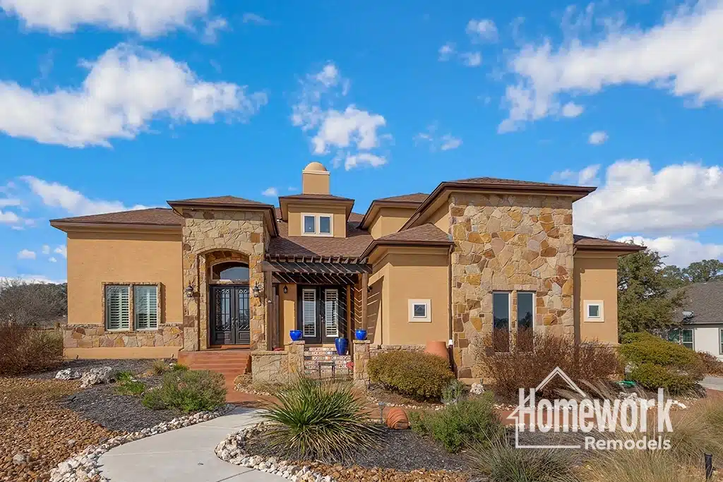 A modern southwestern-style Phoenix home remodel with tan stucco and stone exterior, arched entryway, blue pots by the door, and landscaped front yard under a partly cloudy sky. “Homework Remodels” logo is in the bottom right corner.