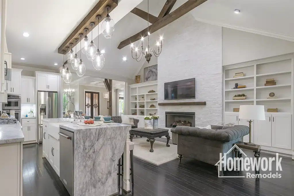 A modern, open-concept Tempe kitchen and living room featuring white cabinets, marble countertops, and exposed wood beams—an example of how removing load-bearing walls in older homes can create a bright, stylish, and elegantly decorated space.