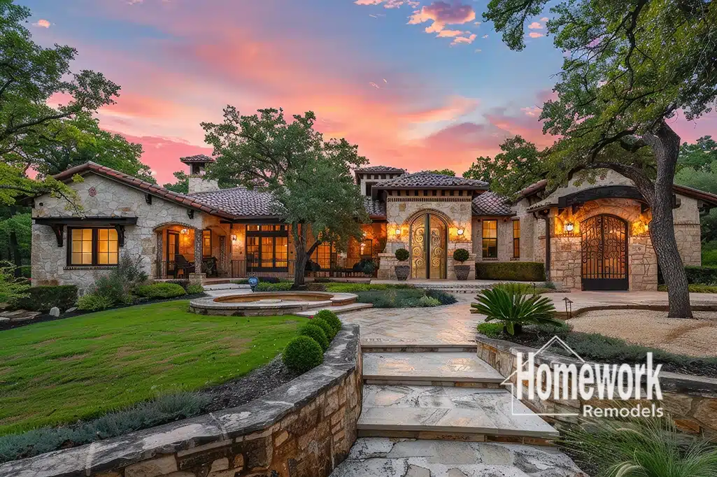 A large, elegant stone house with warm exterior lights, arched windows, and a manicured lawn at sunset. Perfect for ADUs or casitas in Arcadia Lite. The logo Homework Remodels appears in the bottom right corner.