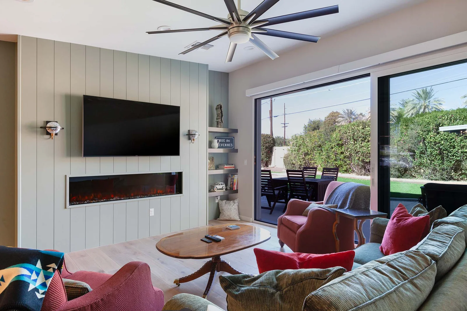 Living room with a mounted television above a linear electric fireplace, facing a sectional sofa, a coffee table, and sliding glass doors leading to a patio.