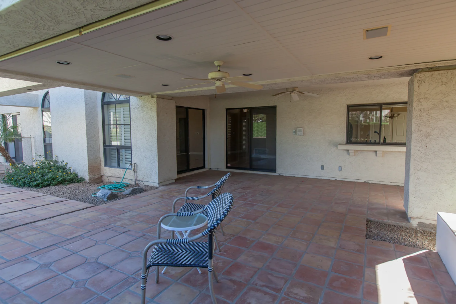 Covered backyard patio before remodeling with worn terra-cotta paving and an older sliding glass door