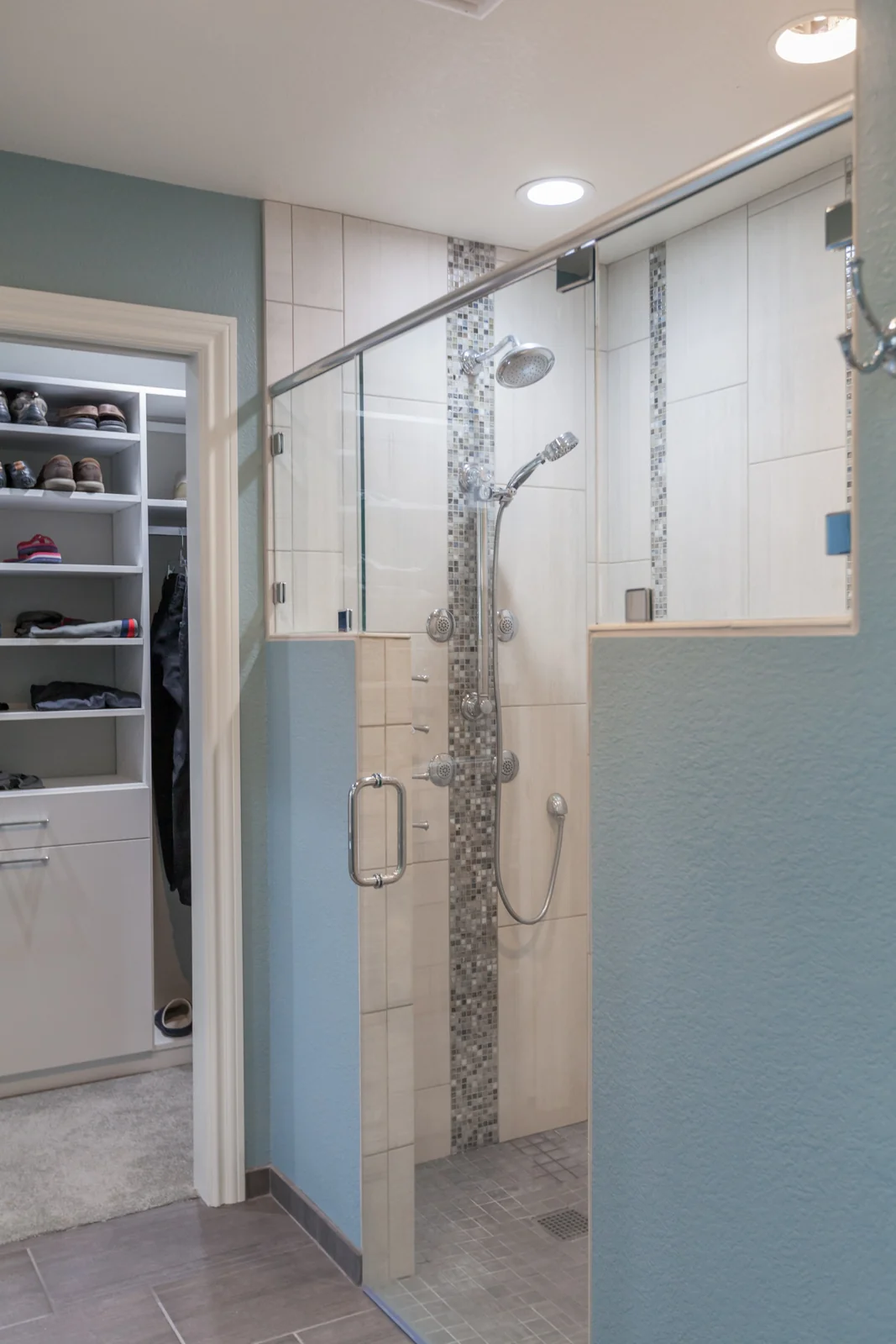 Curbless primary shower with clear glass, vertical tile, chrome fixtures, and an adjacent clothes closet