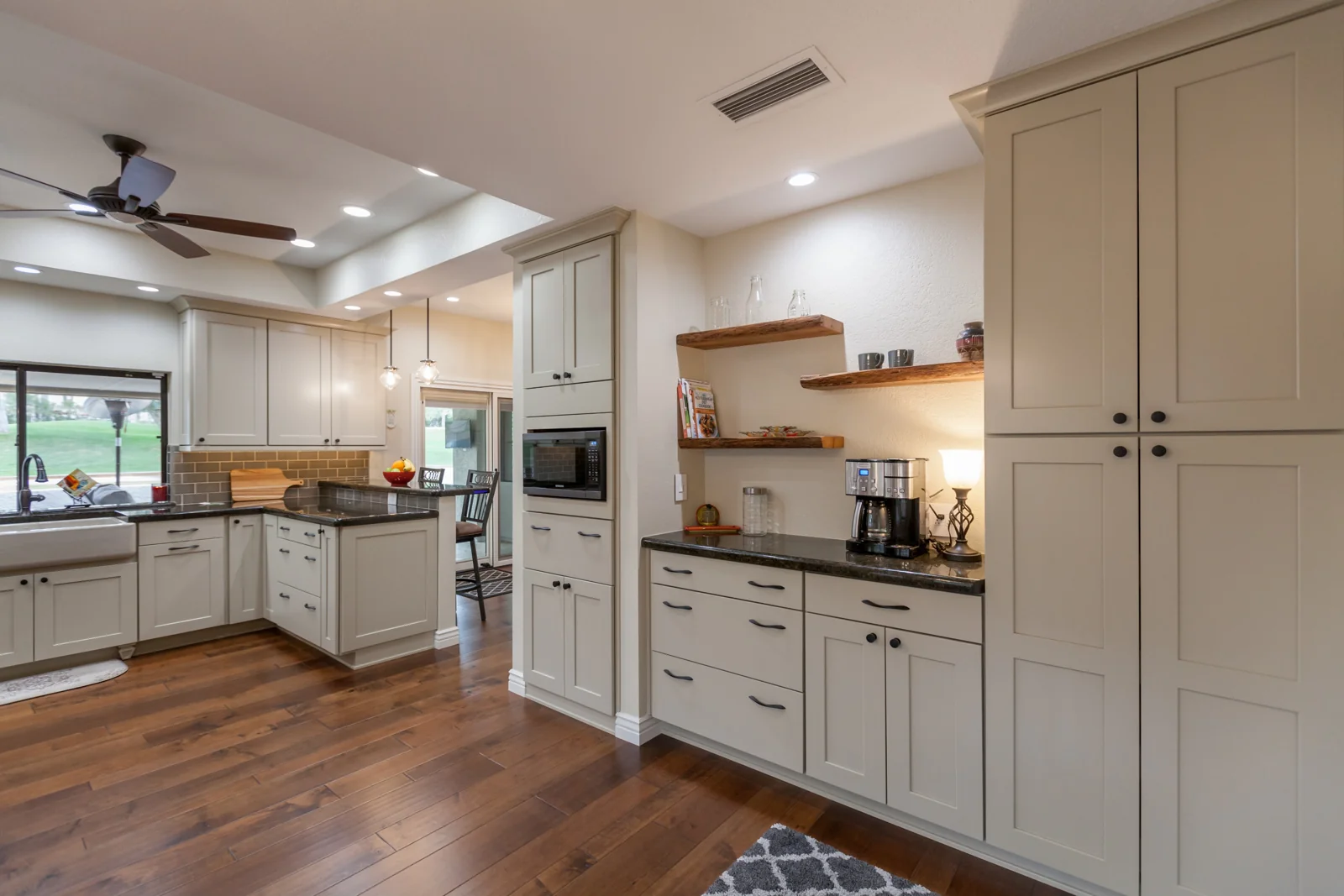 Warm gray kitchen cabinetry with a tall pantry, cooking appliances, and reclaimed wood shelves at the coffee area