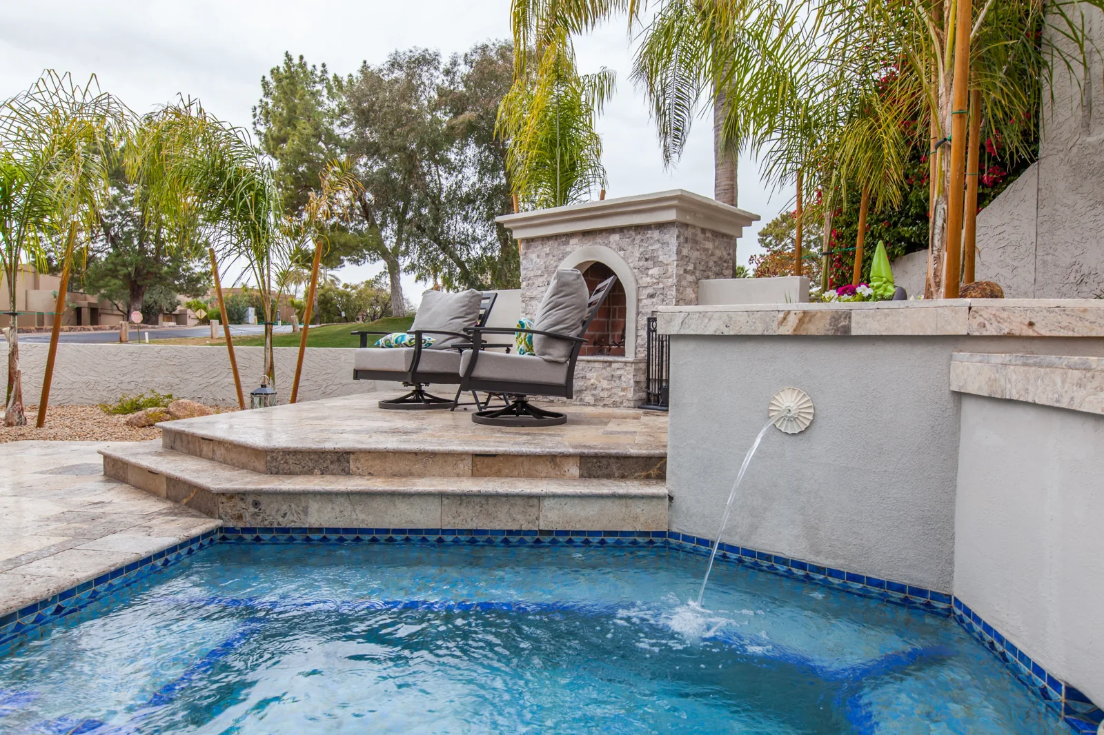 Outdoor stacked stone fireplace on a raised travertine patio beside the spa