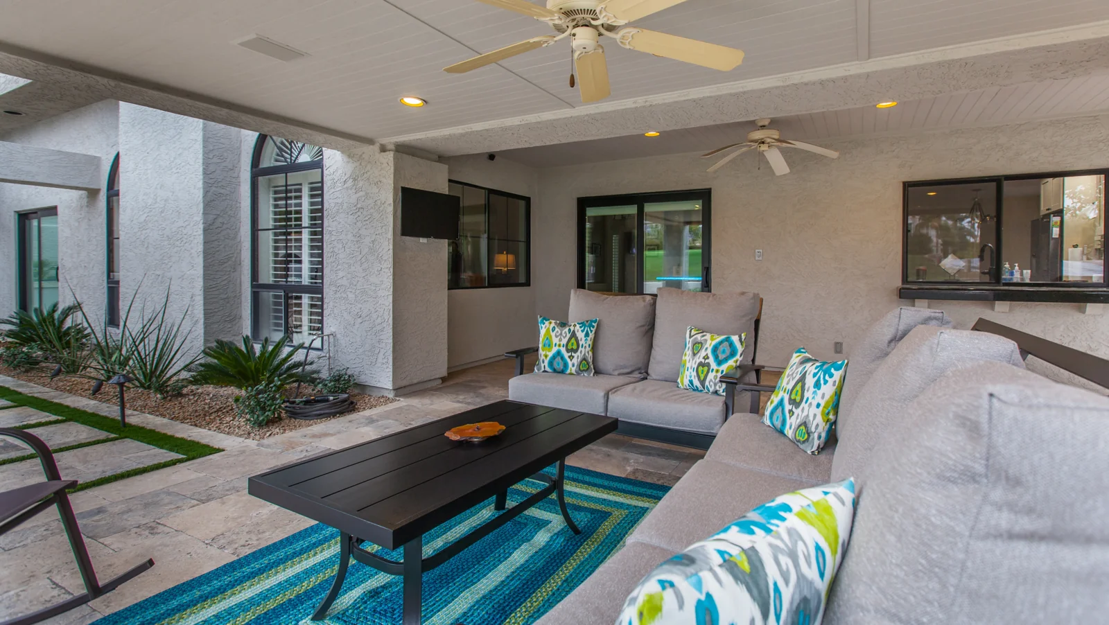 Renovated covered patio with silver travertine paving, seating, a serving counter, and refreshed landscaping