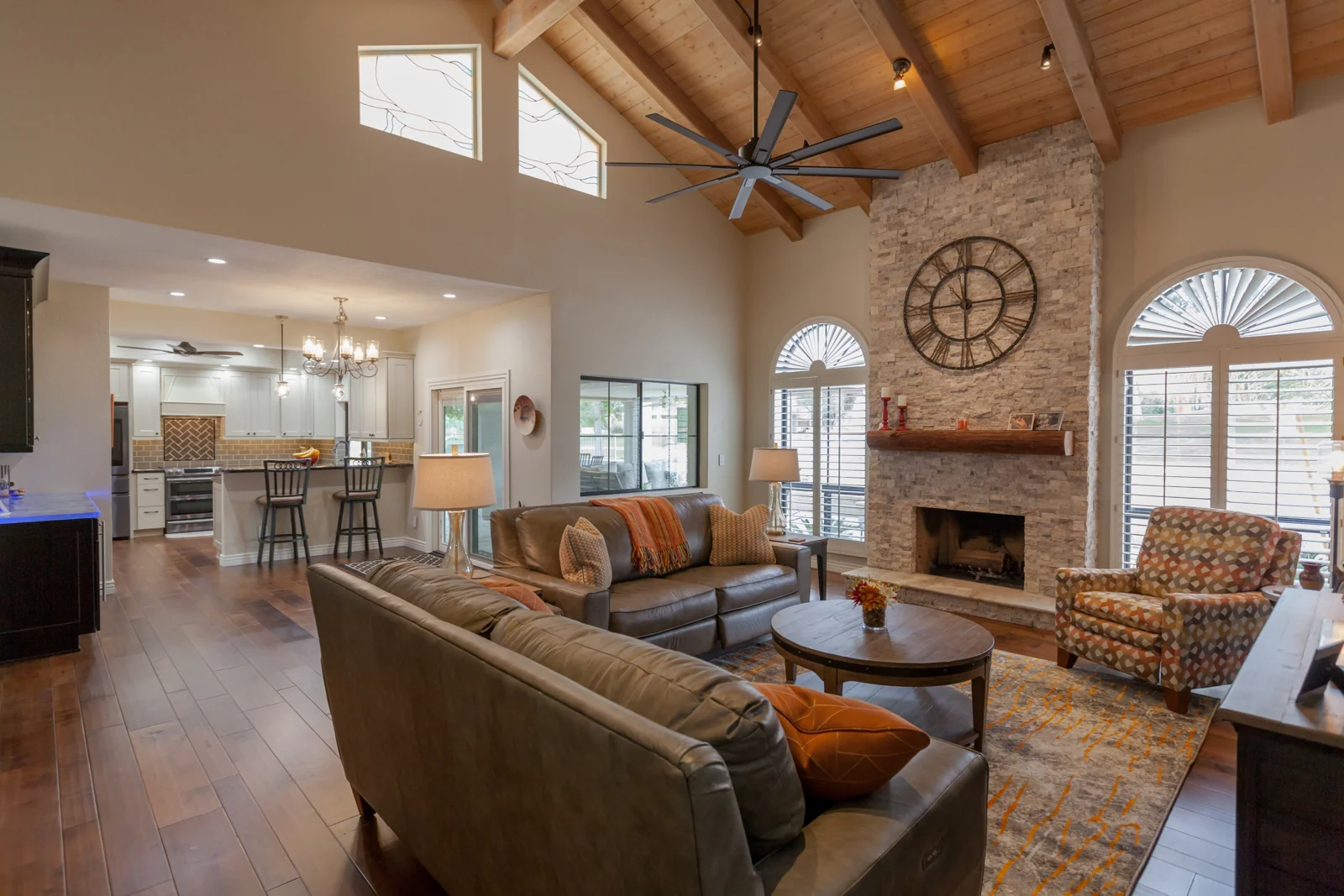 Remodeled Biltmore Phoenix living room with exposed wood ceiling beams, a stacked stone fireplace, engineered wood floors, and an adjoining updated kitchen