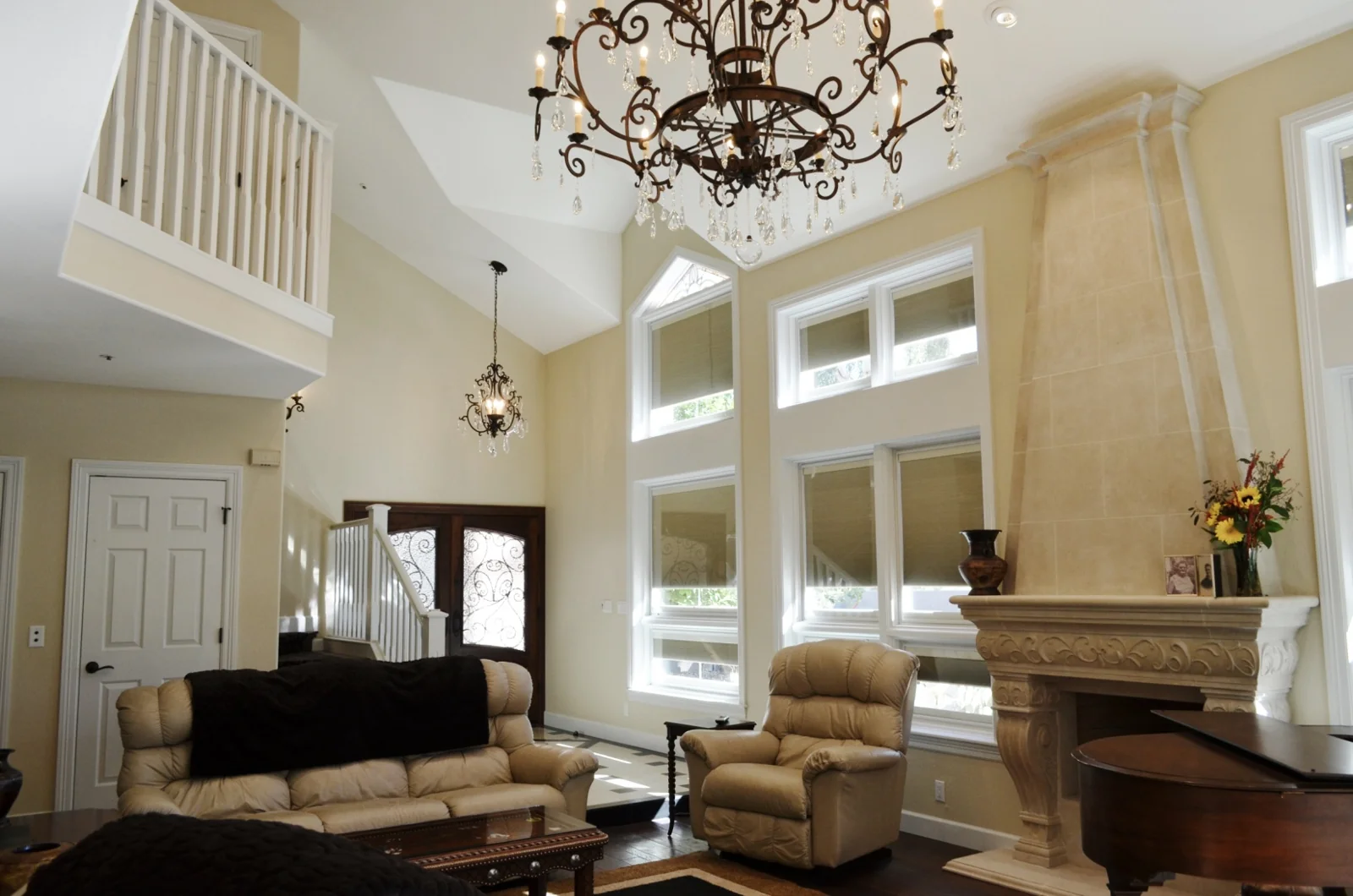 Remodeled Gainey Ranch great room in Scottsdale with a carved stone fireplace, tall trimmed windows, a chandelier, piano, and seating