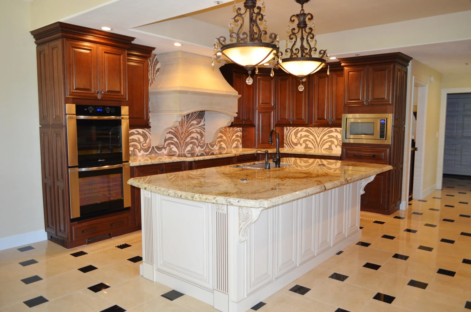 Kitchen with dark wood cabinetry, an island with a light granite countertop, and two ornate hanging light fixtures.