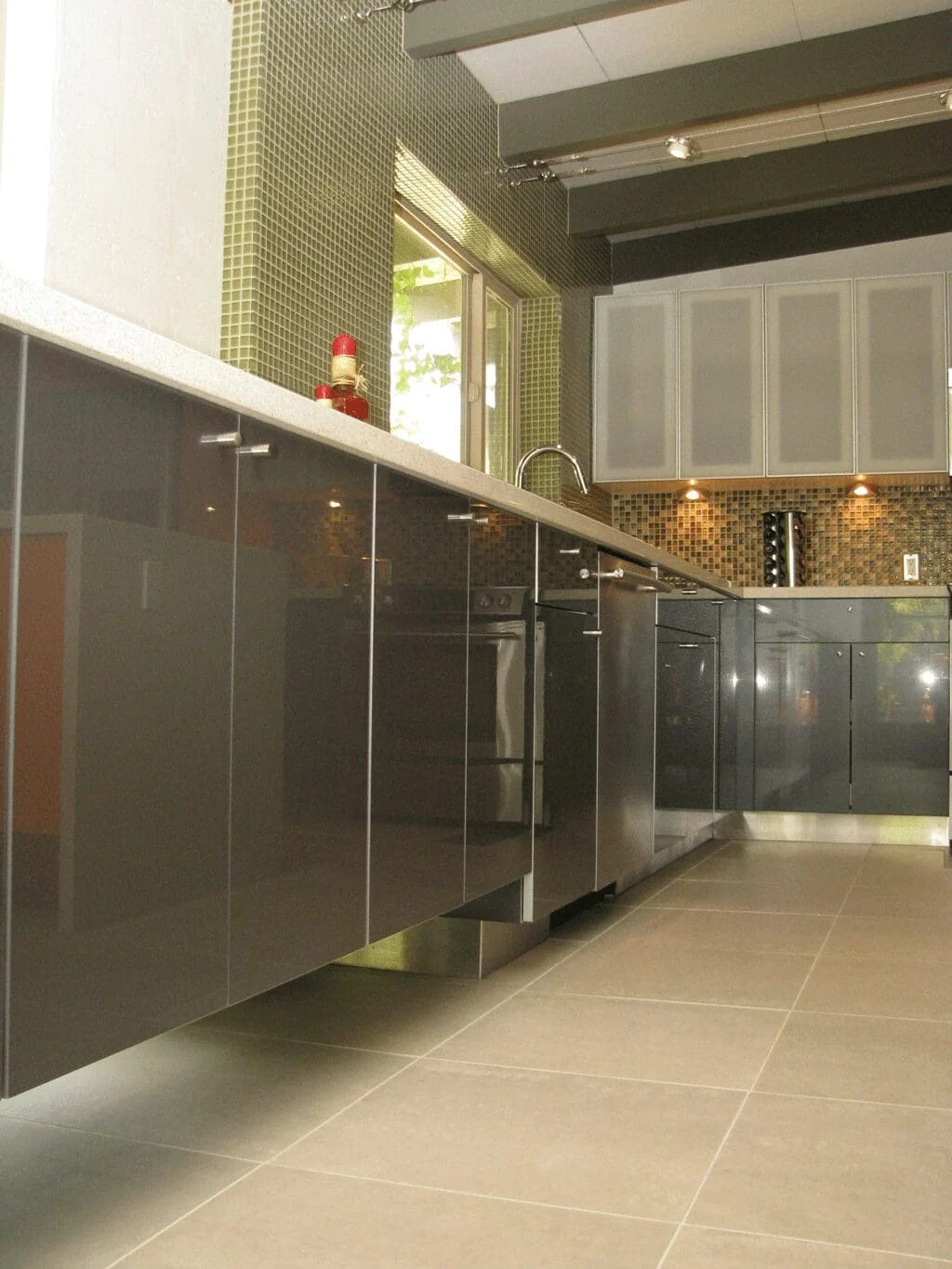 Glossy gray kitchen cabinets, stainless steel toe kicks, and large-format tile flooring