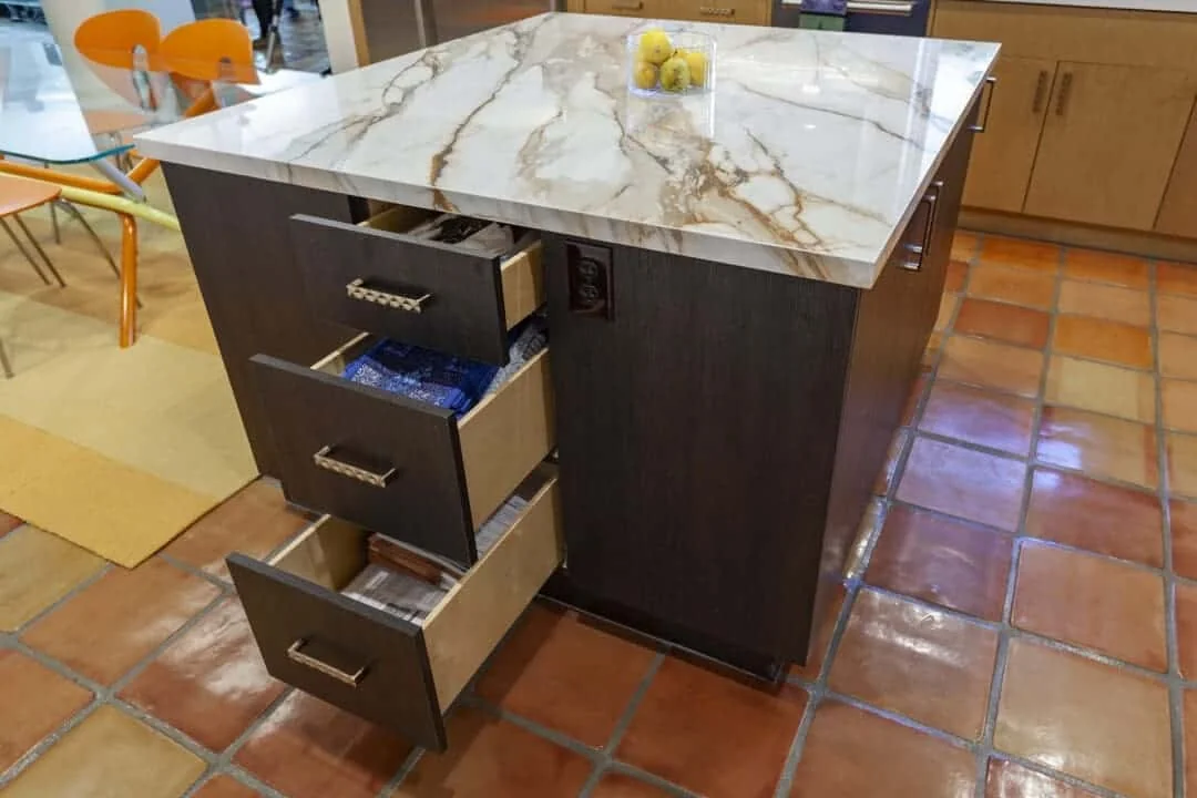 Dark kitchen island with open divided drawers organizing utensils beneath the porcelain counter