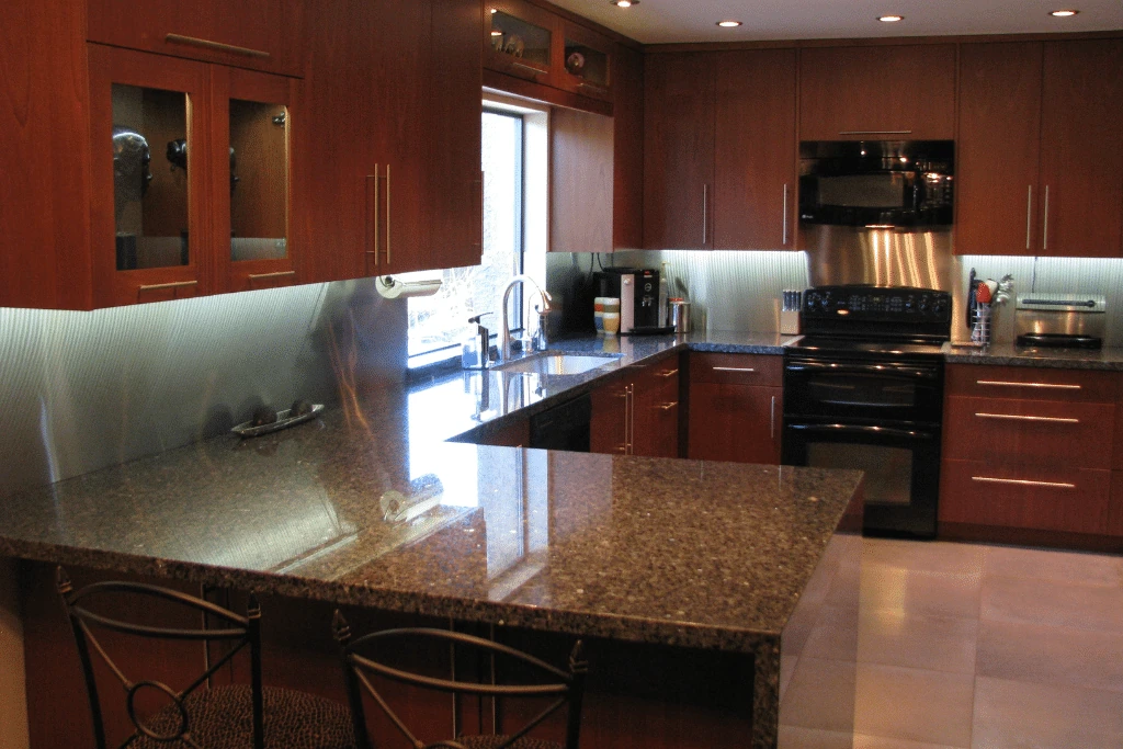 Completed kitchen with warm wood slab-front cabinetry, a dark polished peninsula, black appliances, and lighting beneath the wall cabinets