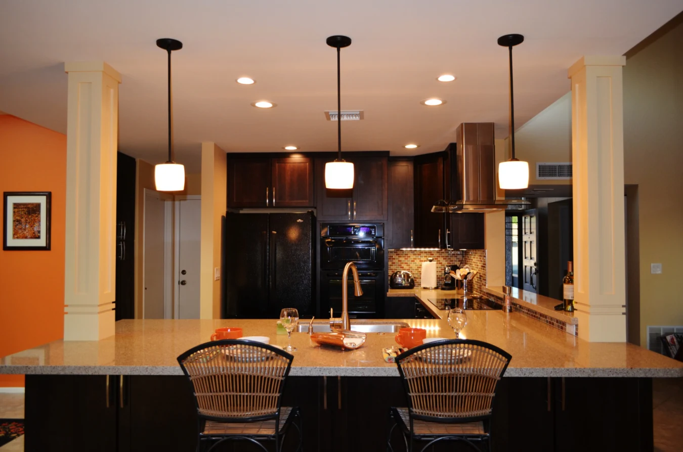 Completed open-concept Phoenix kitchen with espresso cabinets, quartz peninsula seating, pendant lights, and retained tile flooring
