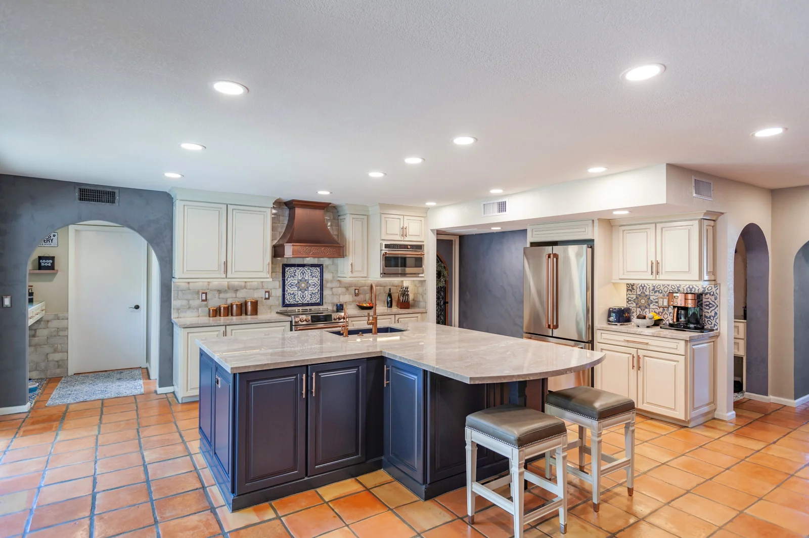 Mediterranean kitchen remodel in Phoenix with cream cabinets, a navy island, copper range hood, quartzite countertops, and Saltillo tile