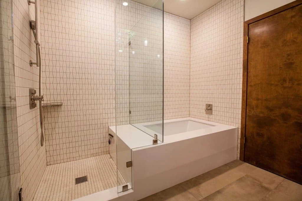 Completed bathroom with a frameless glass shower, geometric wall tile, white tub surround, and wood door
