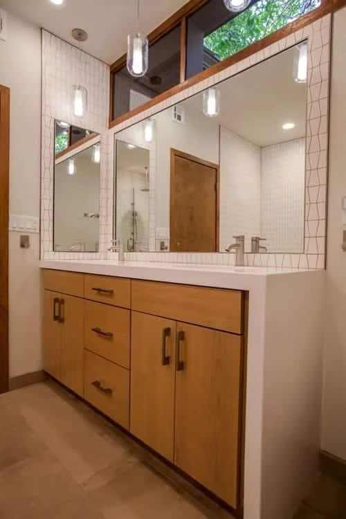 Portrait view of the wood vanity, white counter, brushed-metal fixtures, and geometric tile behind the mirror