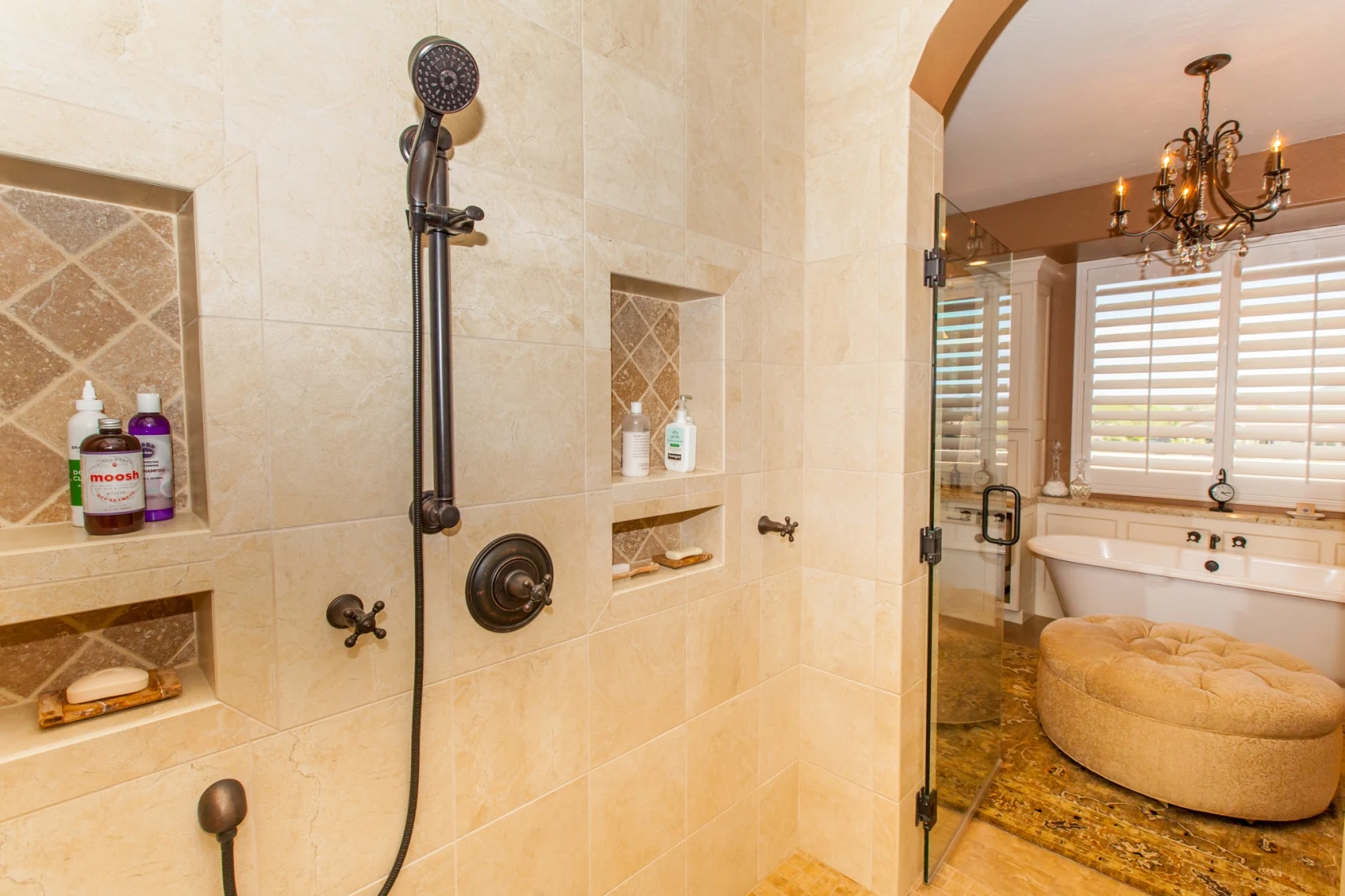 View from the remodeled shower toward the traditional bathroom, showing controls near the entry and a hand shower