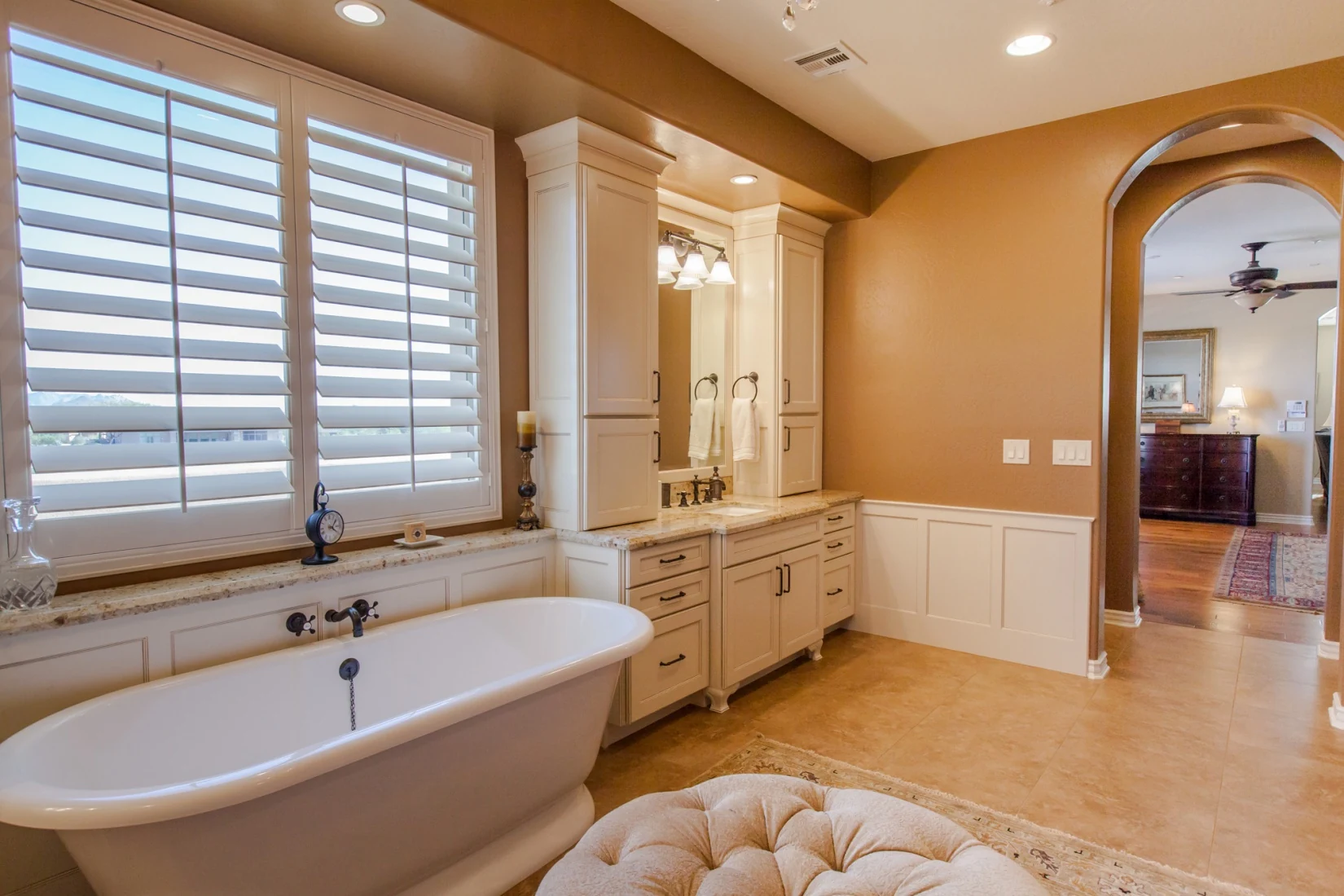 Finished bathroom with a freestanding tub beneath shutters, traditional millwork, and open floor area