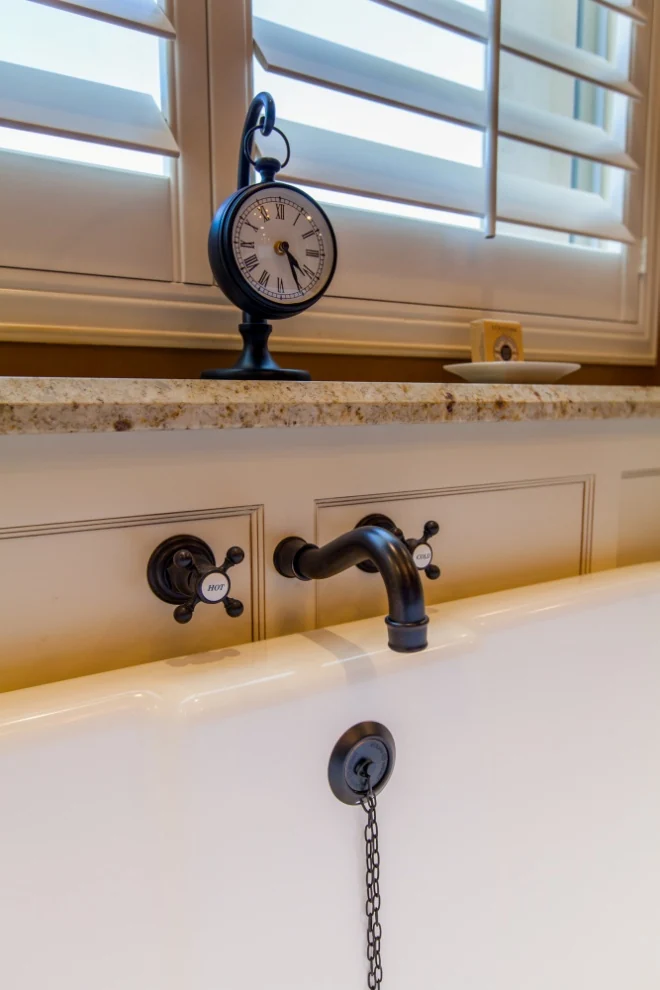 Freestanding tub with oil-rubbed bronze fittings, cross handles, and a paneled shelf below the window