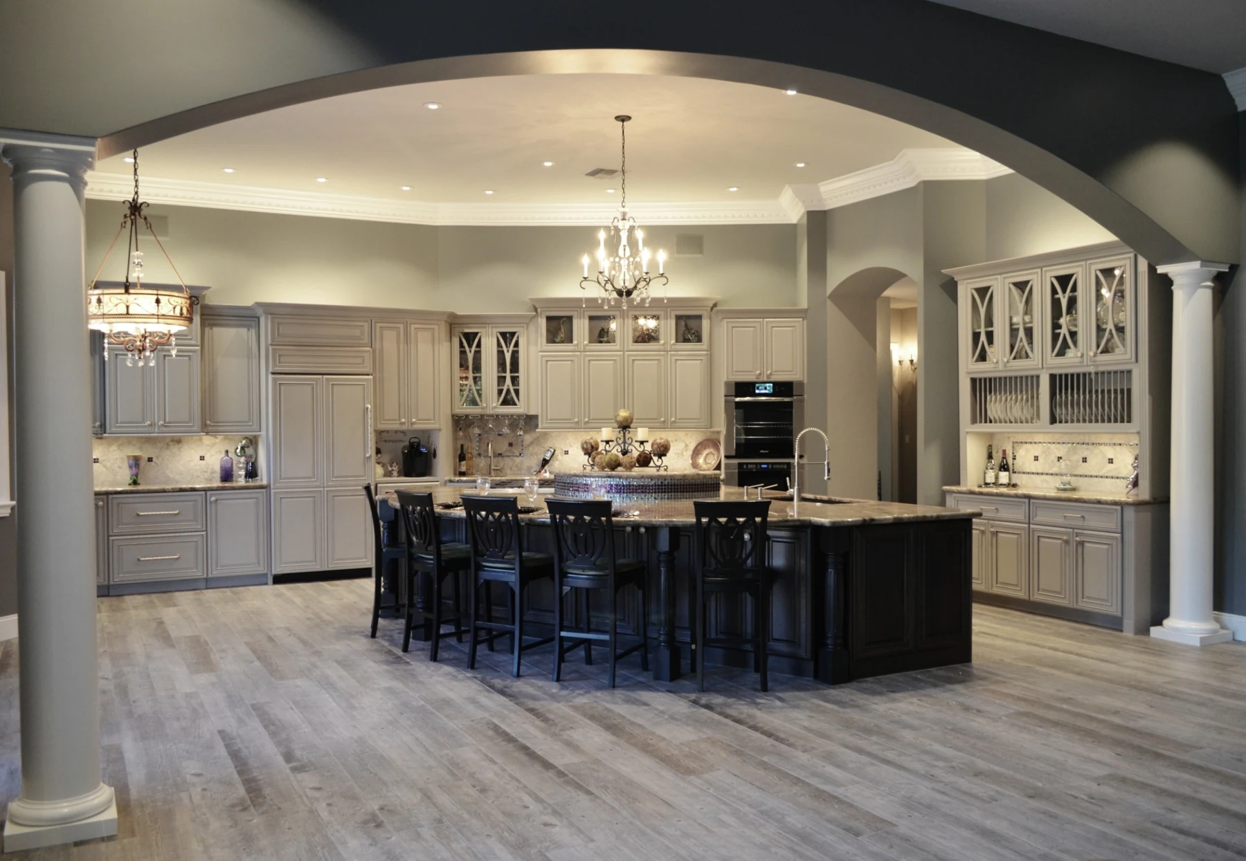 Completed Tempe kitchen framed by an archway and columns, with gray custom cabinets and a charcoal cherry island