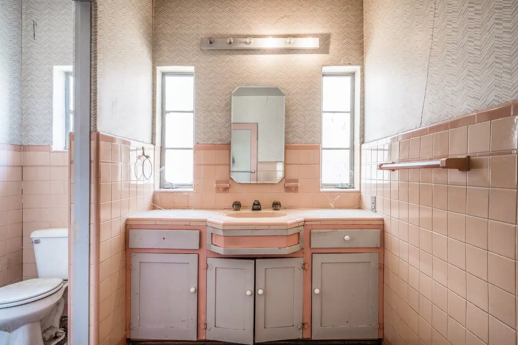 Original pink-tiled bathroom vanity beneath two windows
