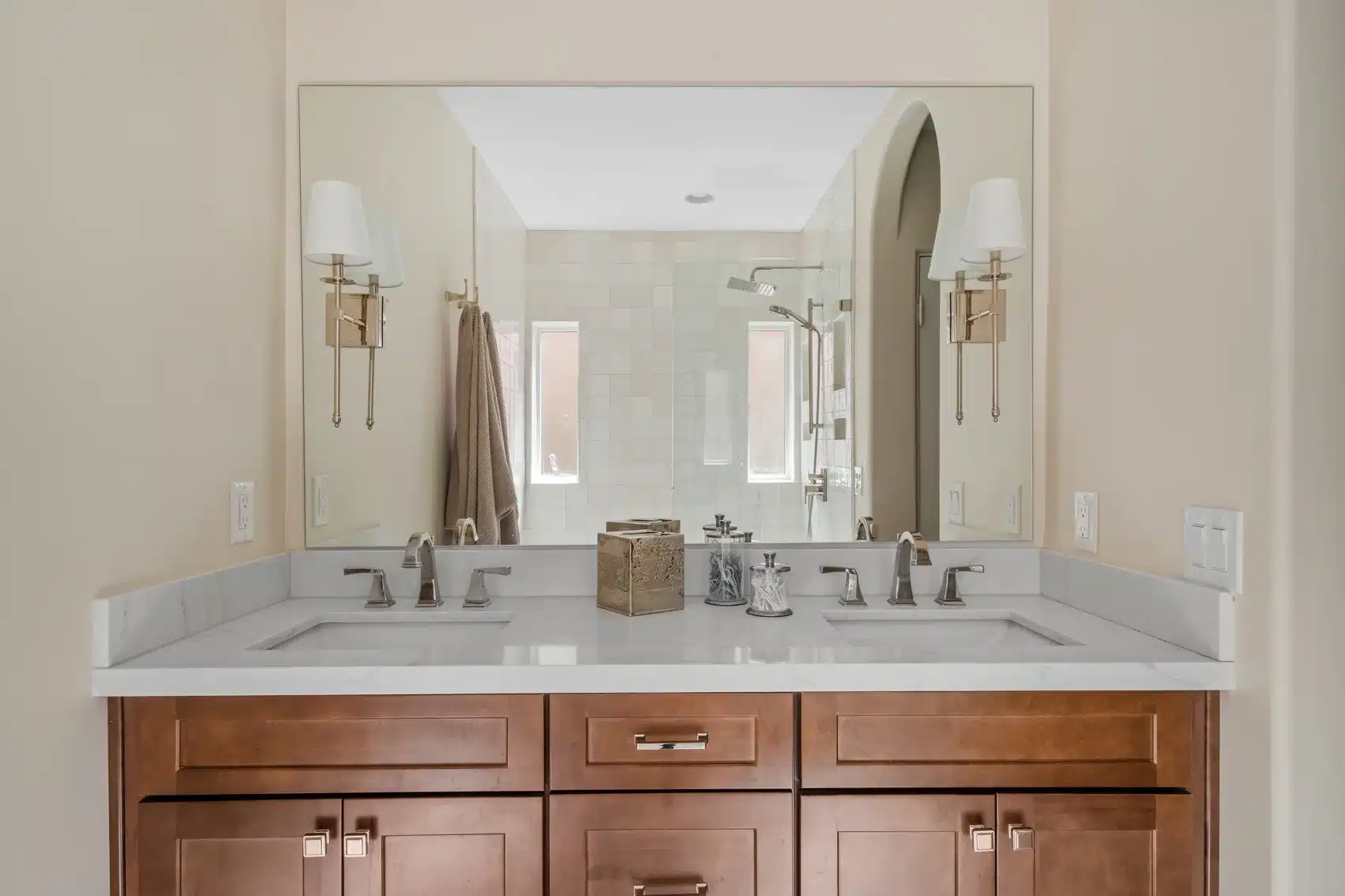 Completed double vanity with wood cabinetry, quartz countertop, polished nickel fixtures, and mirror-mounted sconces