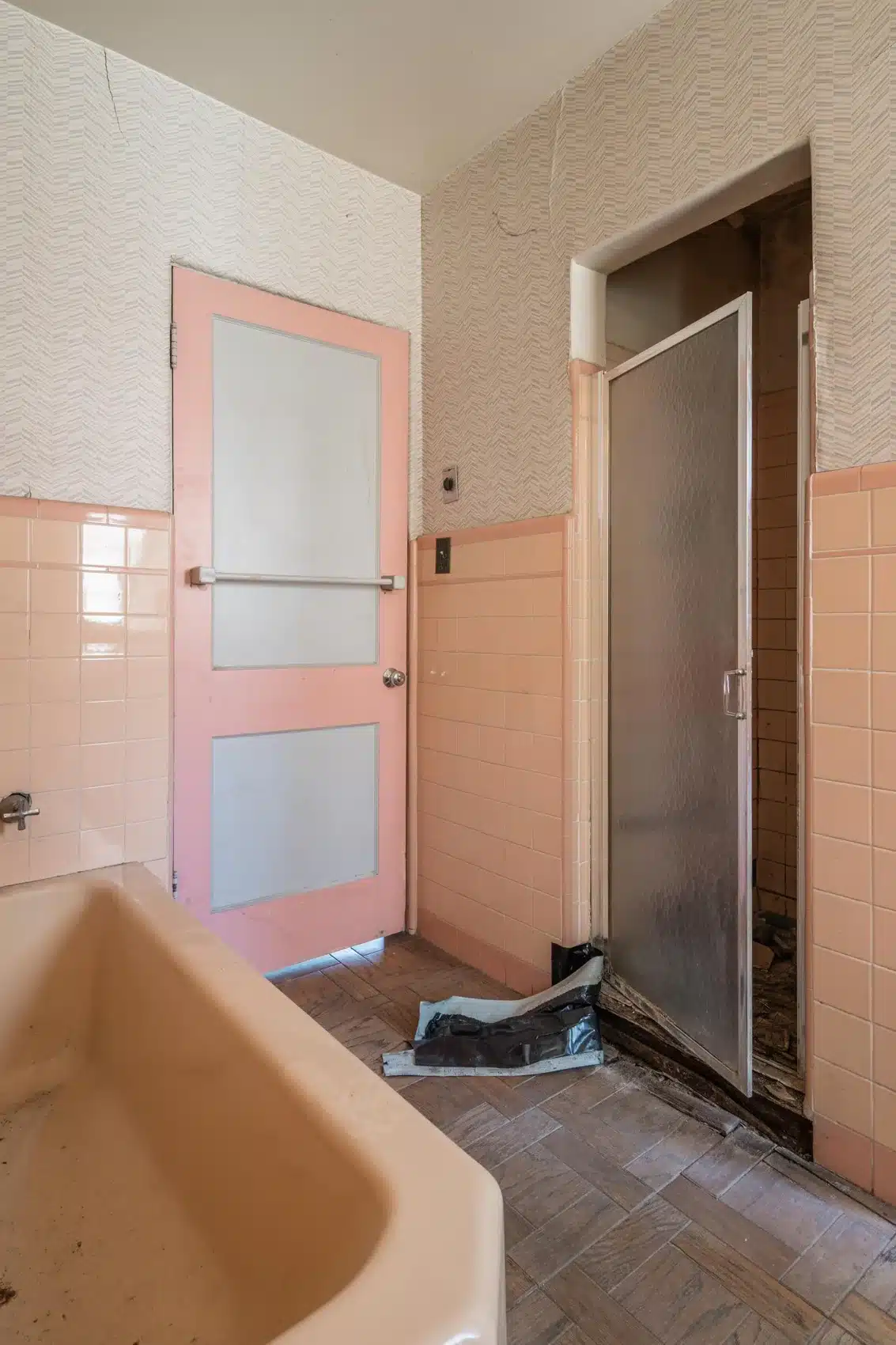 Original tub and pink-tiled bathroom beside narrow shower opening