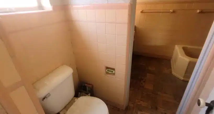 Original toilet compartment with pink wall tile and wall build-out