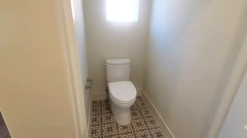 Renovated private toilet compartment with patterned tile floor and window