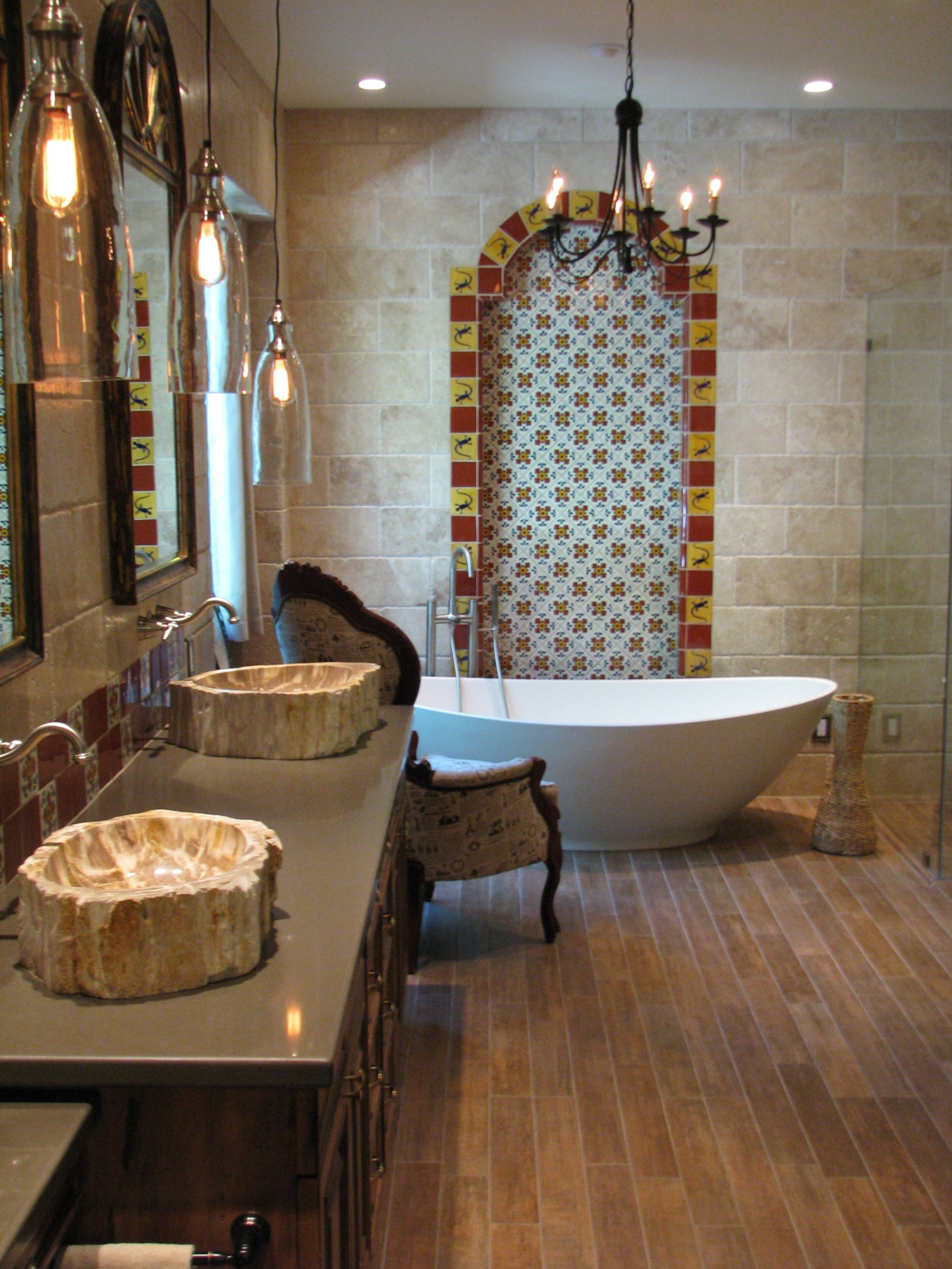 Completed Spanish Colonial bathroom with travertine walls, patterned tile behind a freestanding tub, and petrified wood sinks