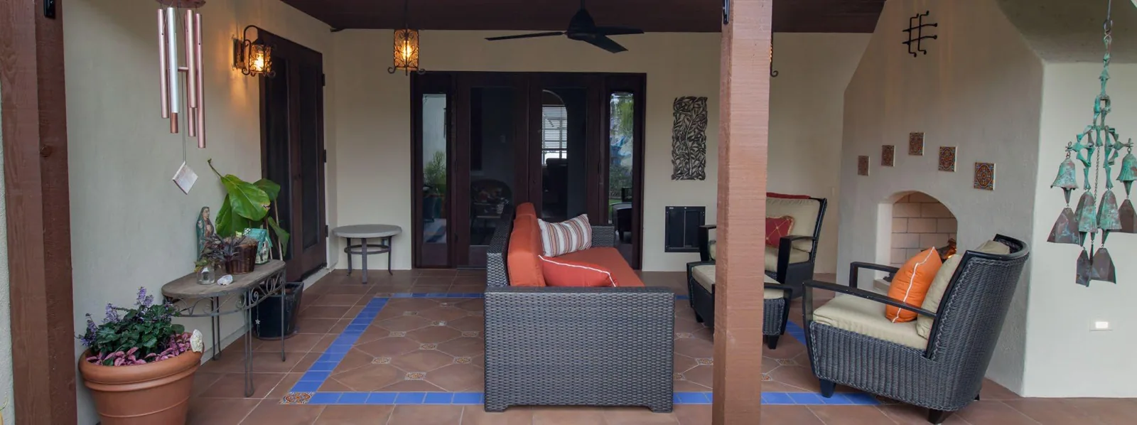 Covered outdoor seating facing the sunroom doors with patterned porcelain flooring and a fireplace at the side