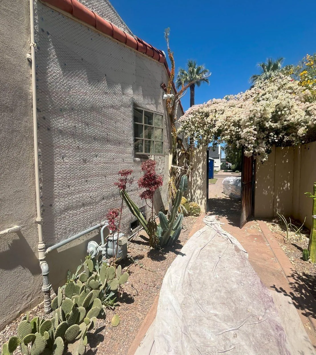Exterior side wall prepared for stucco restoration beside a garden walkway