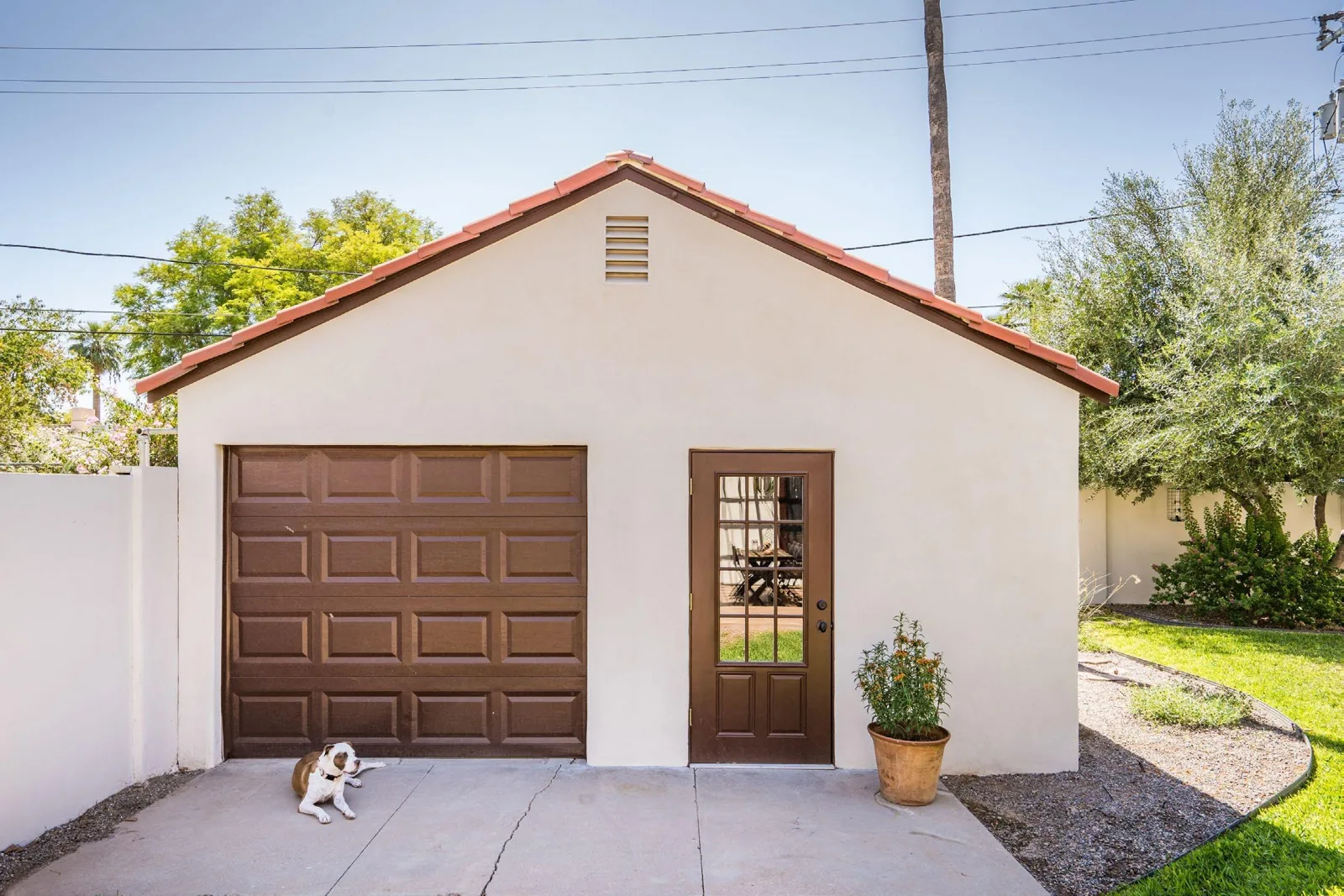 Restored garage with cream stucco, brown garage door, glazed entry door, and gable vent