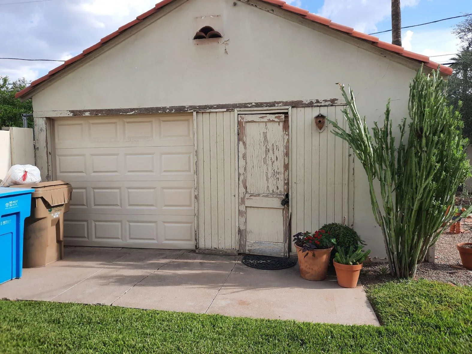 Detached garage before renovation with worn stucco, a deteriorated side entry, and aging paint