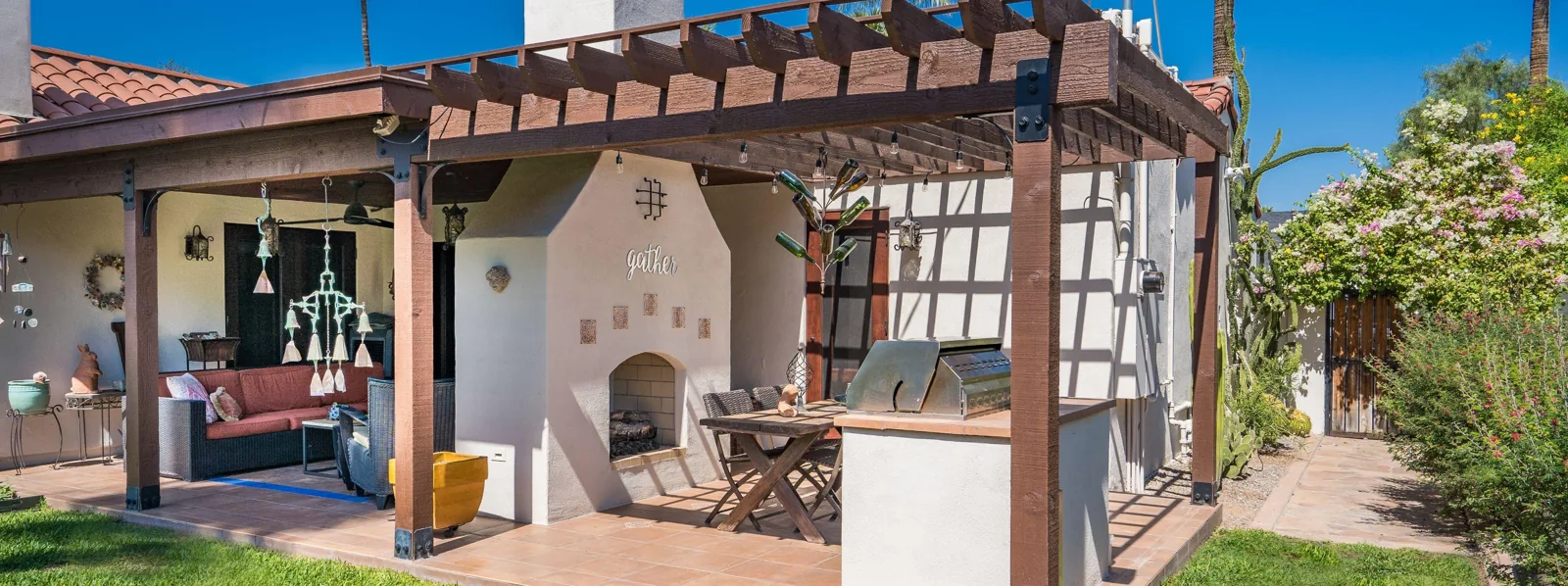 Completed second phase with a cedar pergola, outdoor dining, and a built-in barbecue beside the fireplace