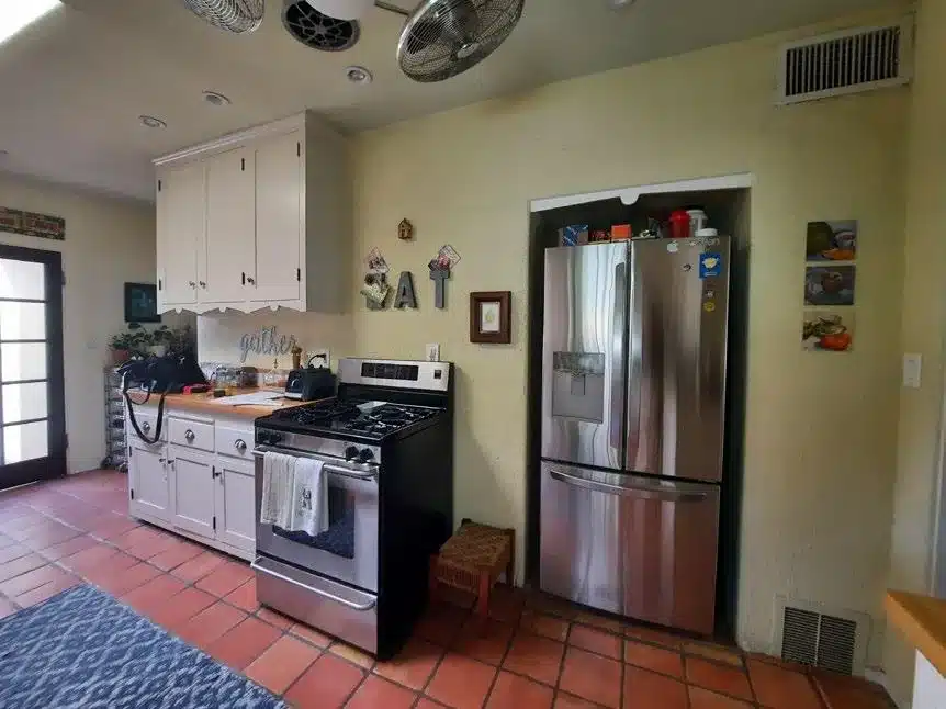 Kitchen before remodeling with a freestanding refrigerator beside the gas range and terracotta floor