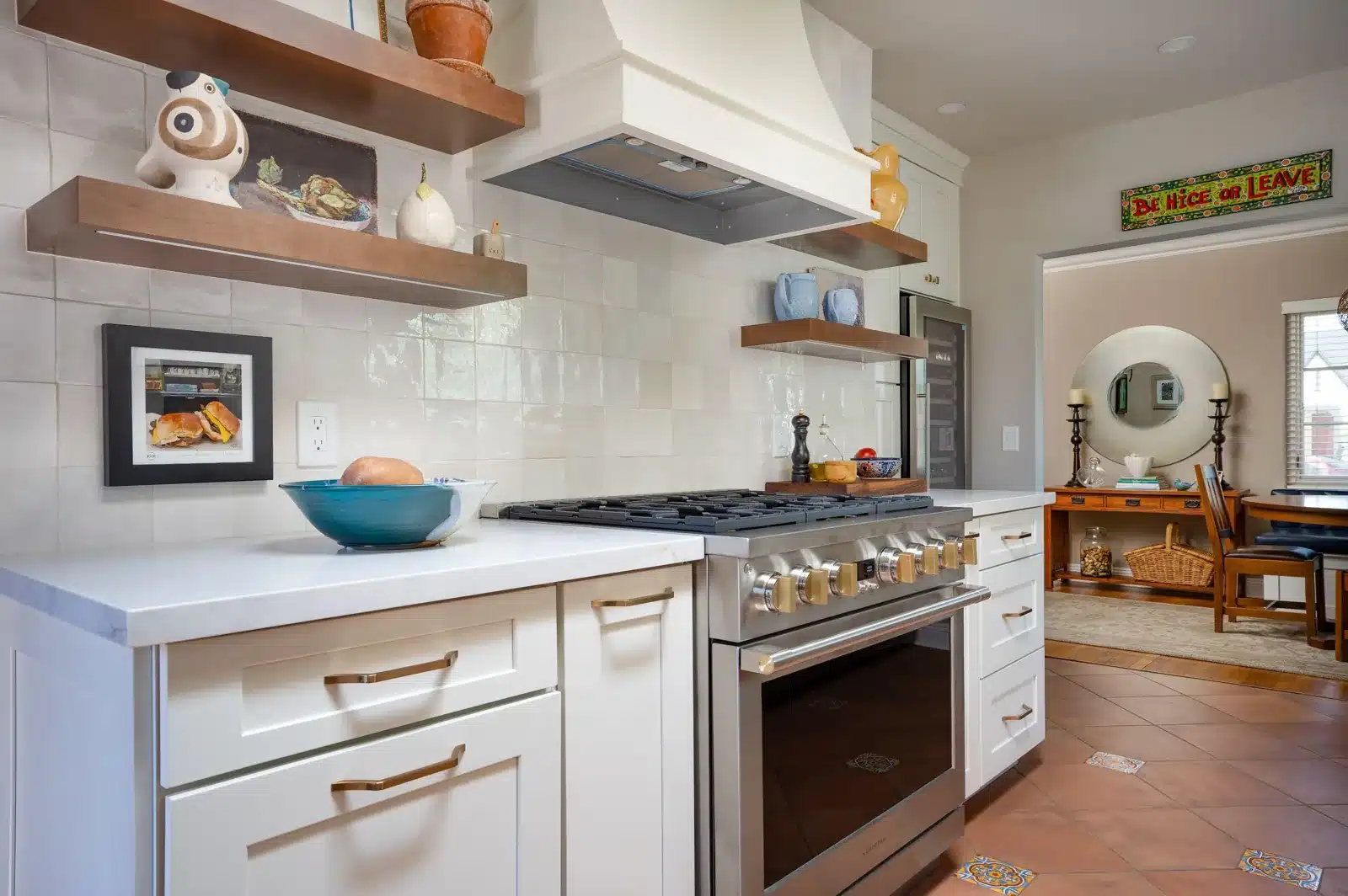 Finished Spanish Colonial kitchen with terracotta-look porcelain floor, a gas range, wood shelves, and an arched doorway