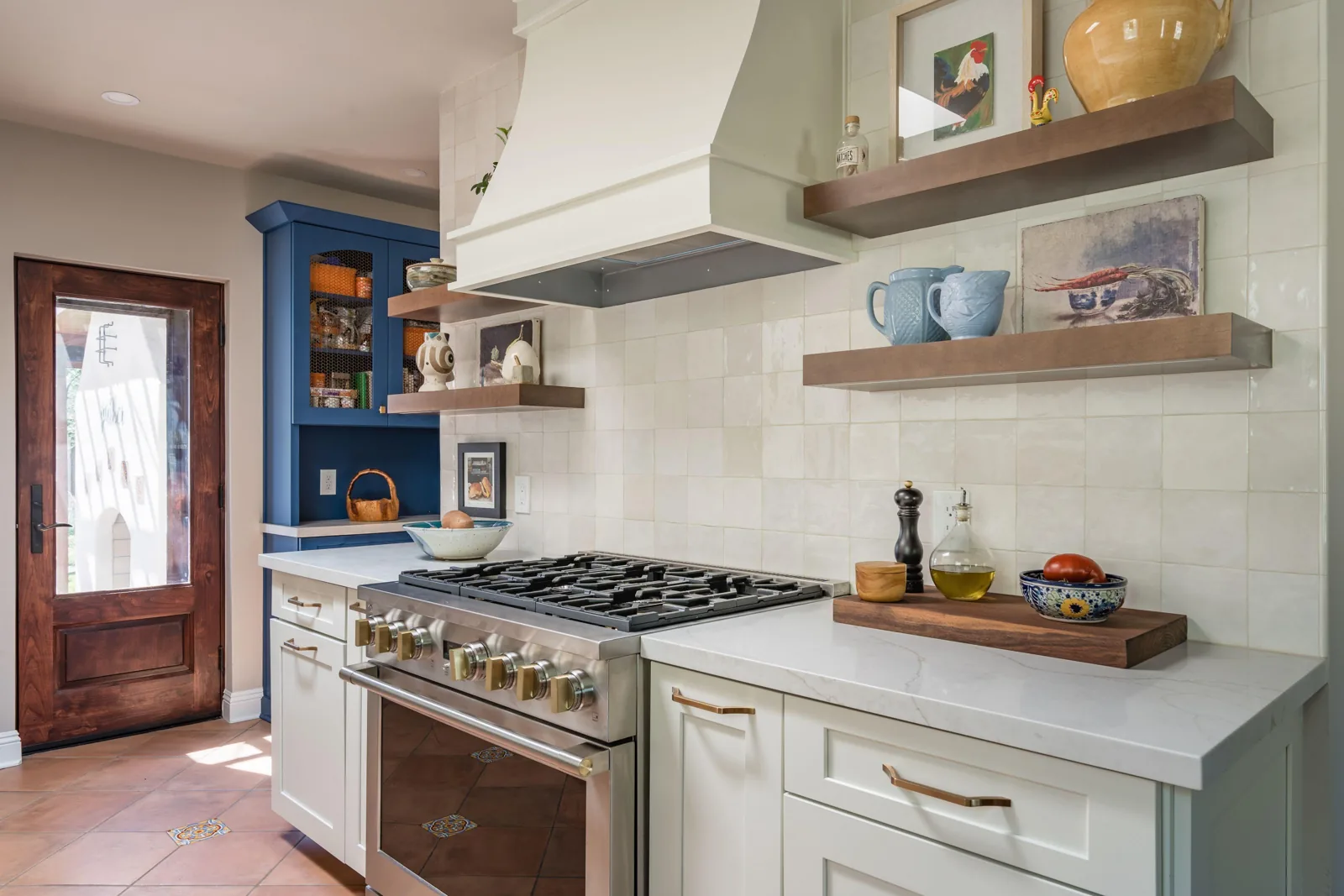 Remodeled gas range wall with a cream hood, floating wood shelves, pull-out cabinetry, and tile backsplash