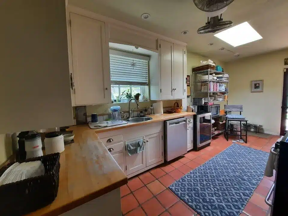 Original kitchen sink wall with a small round sink, low cabinets, and open wire storage